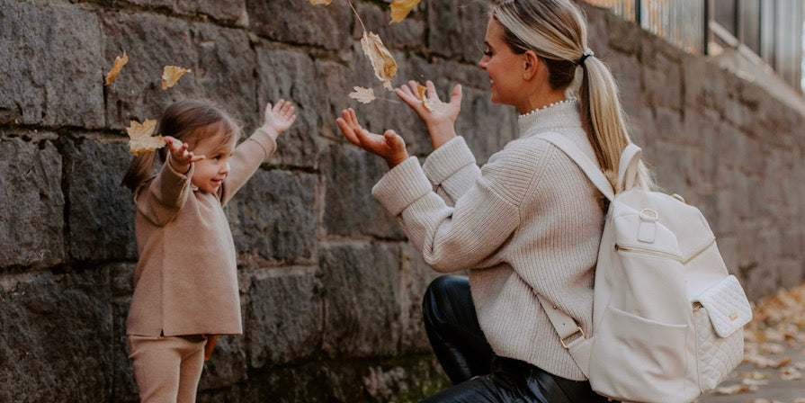 Mom wearing a stylish Luli Bebé diaper bag backpack while holding her child’s hand outdoors.