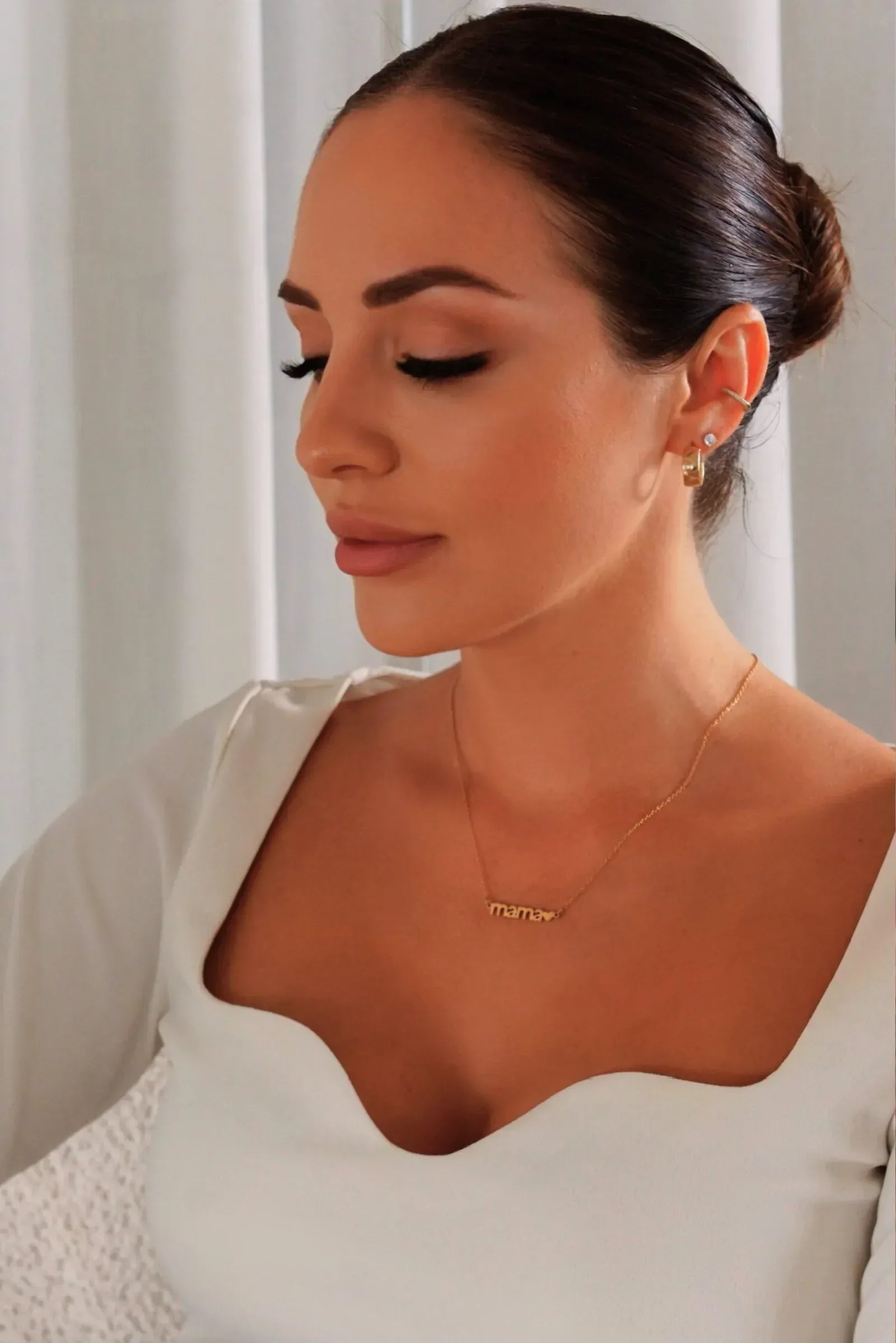 Woman wearing Luli Bebé mama necklace in gold, styled with elegant white dress