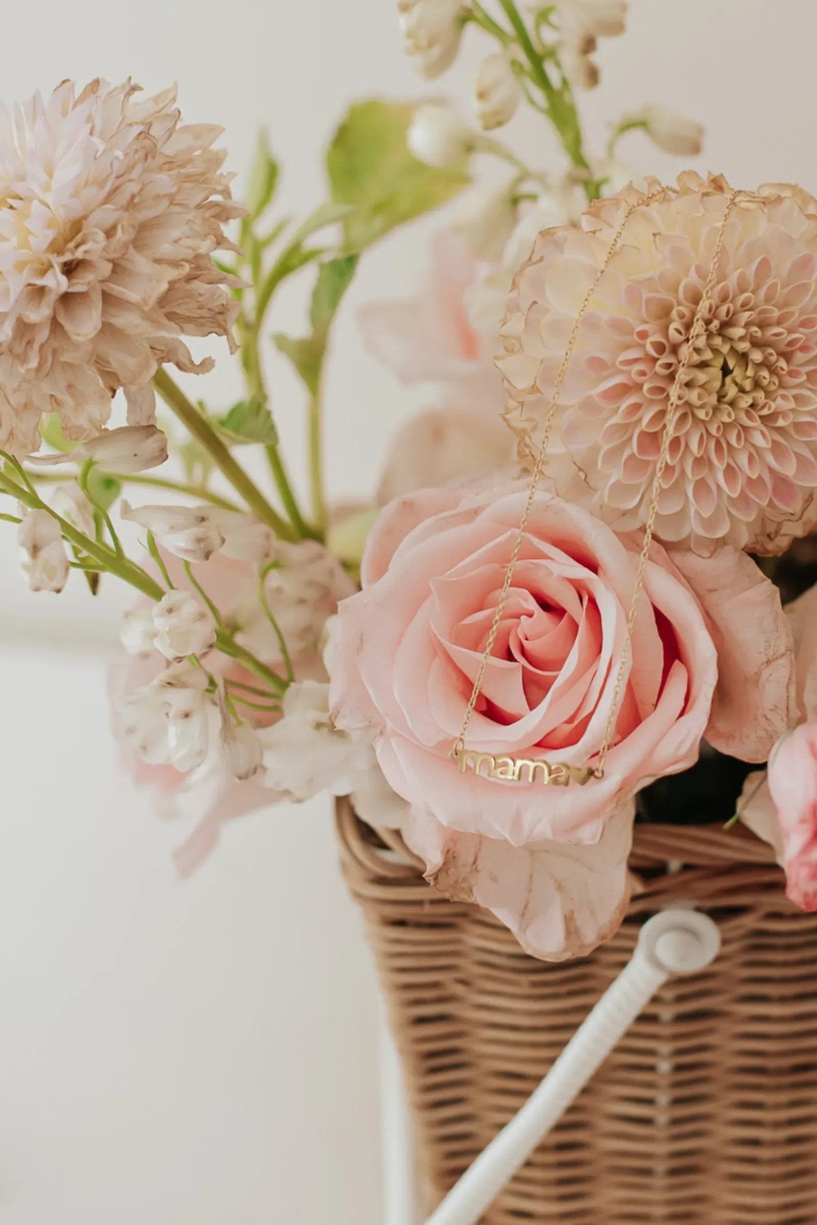Mama necklace draped over pastel pink roses in wicker basket