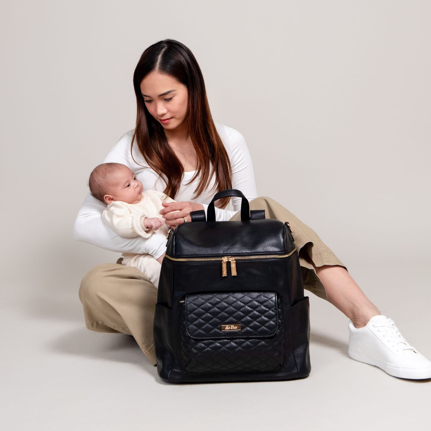 Modern mom holding baby, featuring the black Luli Bebé Signature diaper backpack