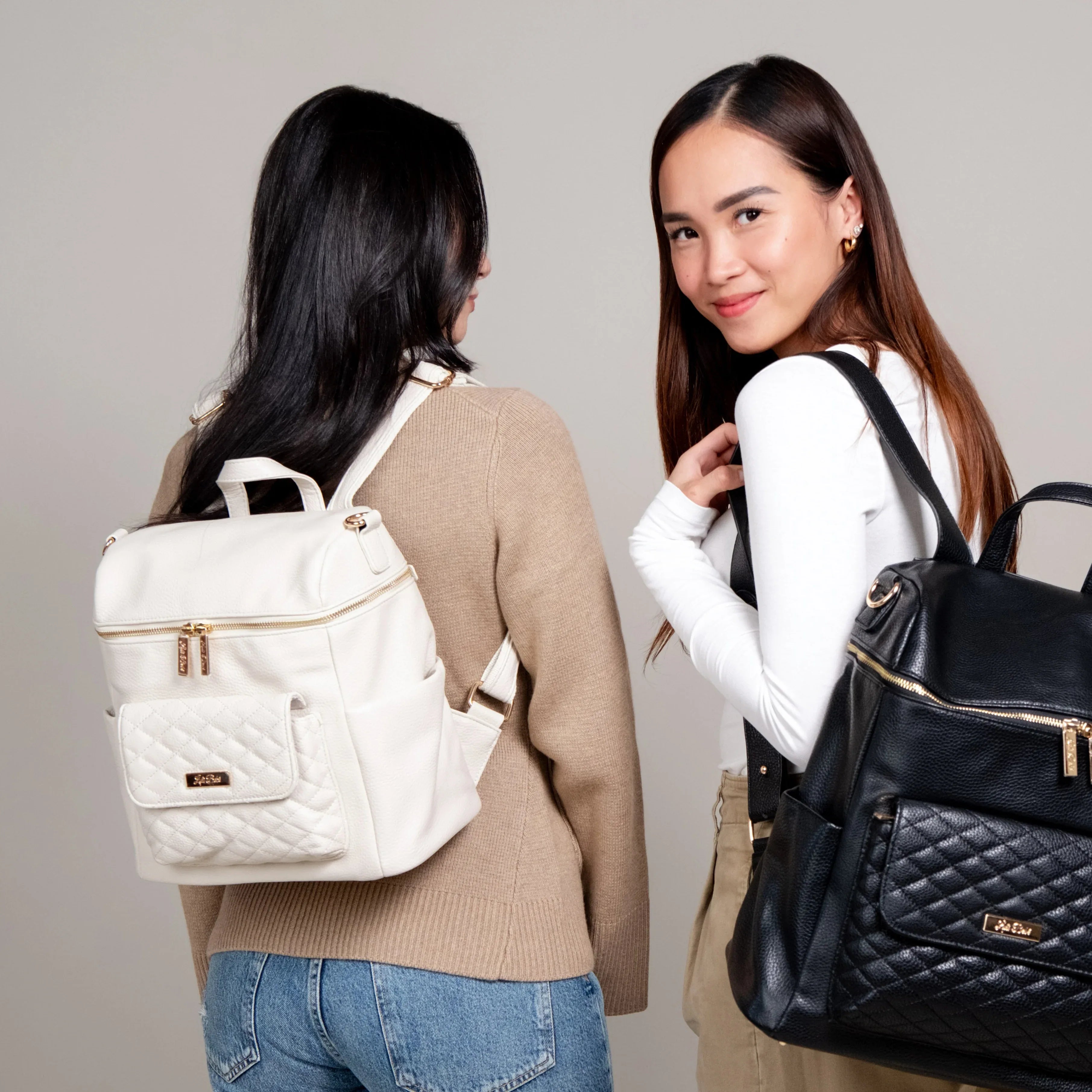 Mom wearing Black Petit diaper bag and mom with Large White Signature diaper bag by Luli Bebe – stylish diaper backpack set with size and style options.