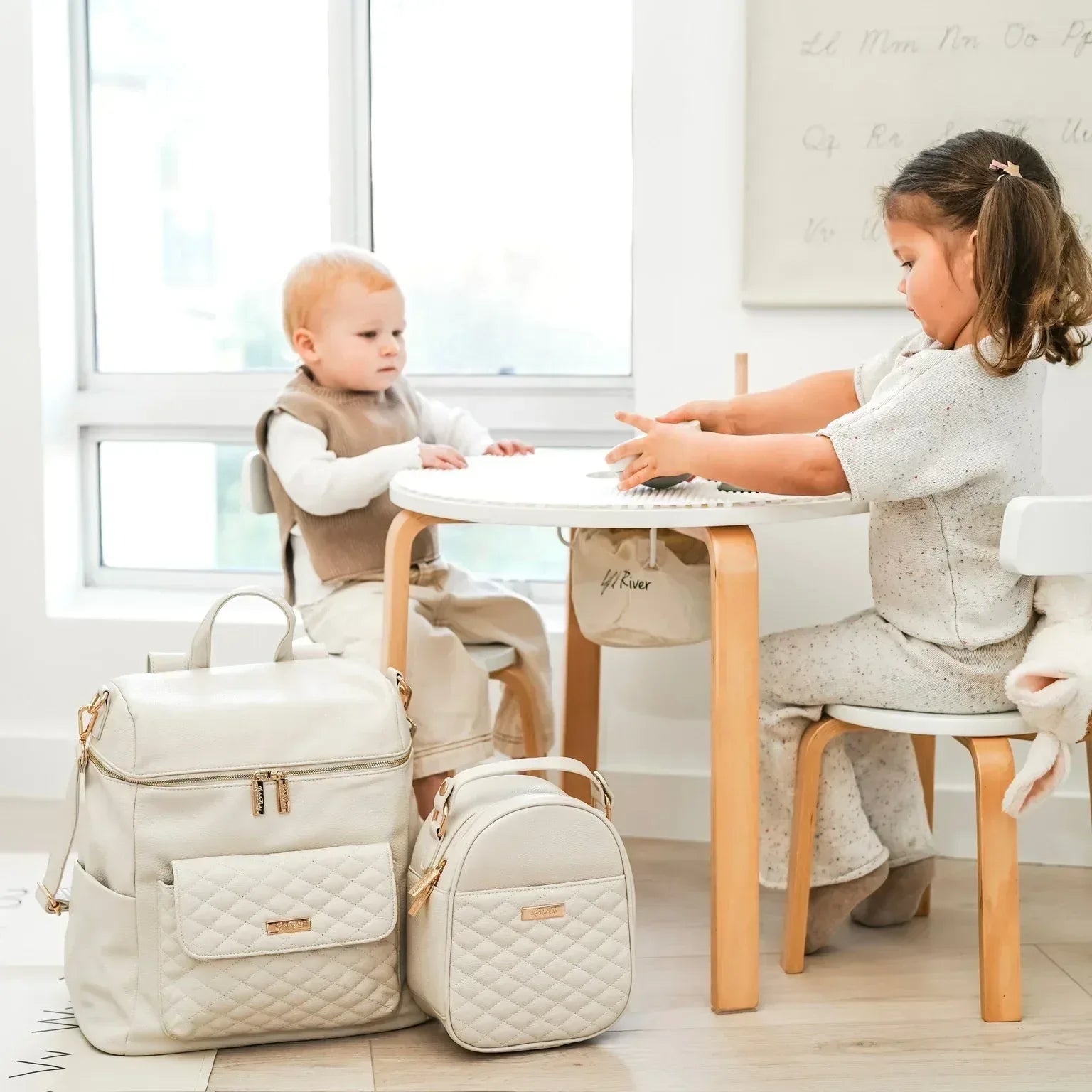 Baby boy and girl playing near Signature Pearl White diaper bag with matching snack bag by Luli Bebe, luxury set for modern moms and travel