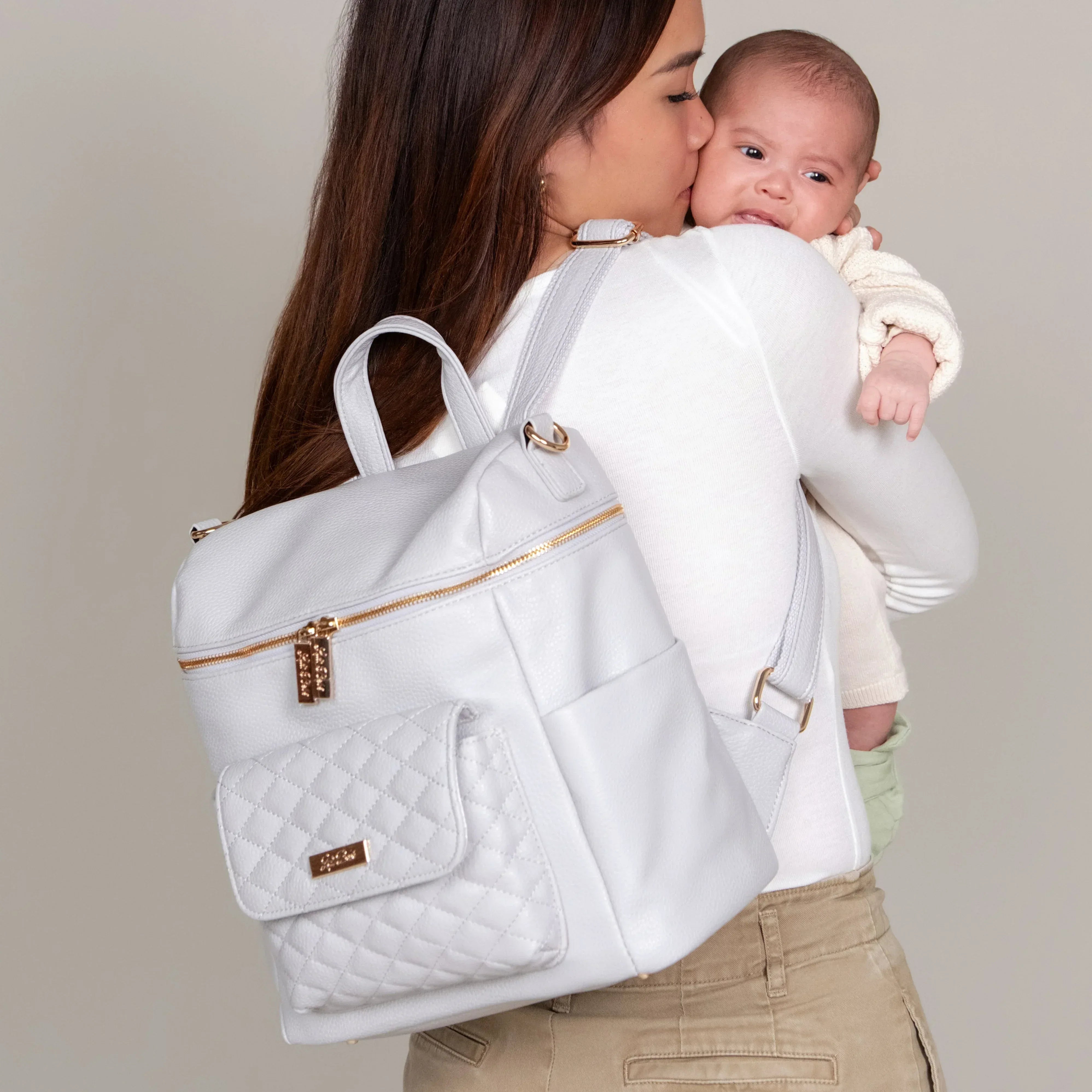 Stone Grey Diaper Bag Backpack – Petit Monaco by Luli Bebe, lifestyle photo of mom holding baby while wearing stylish mini diaper bag backpack