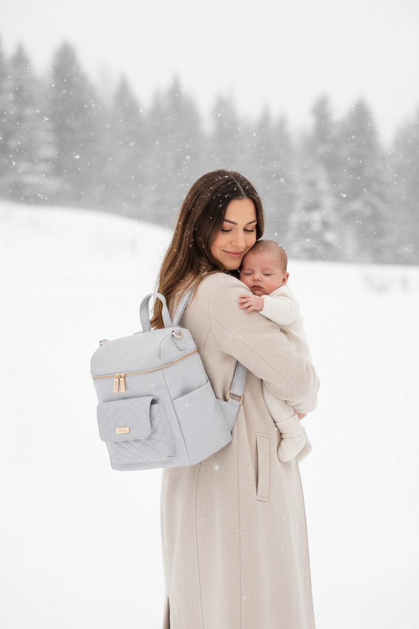 New mom holding baby wearing luxury Luli Bebe diaper bag in snowy winter setting