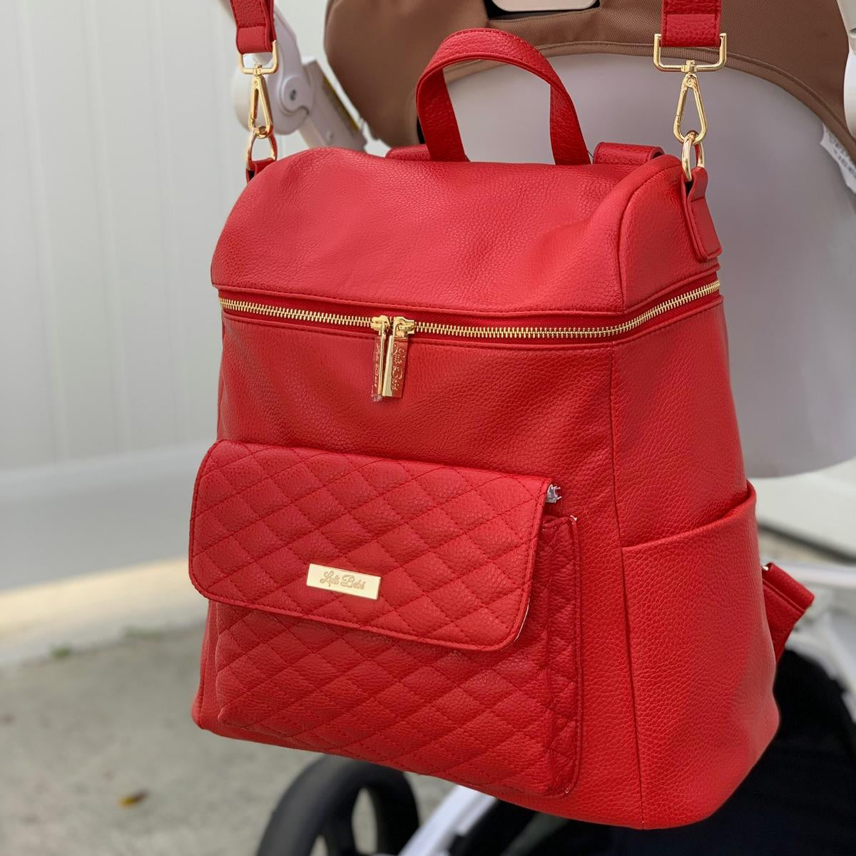 Imperfect Luli Bebé Monaco red vegan leather diaper bag backpack with quilted front pocket and gold hardware.