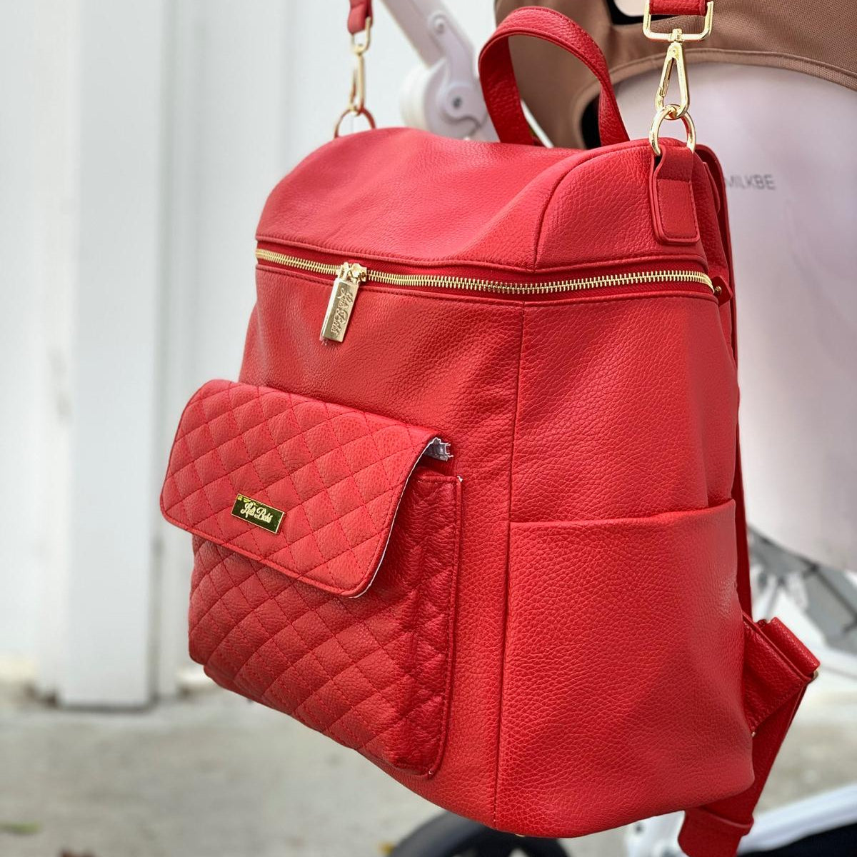 Imperfect Luli Bebé Monaco red vegan leather diaper bag backpack with quilted front pocket and gold hardware.