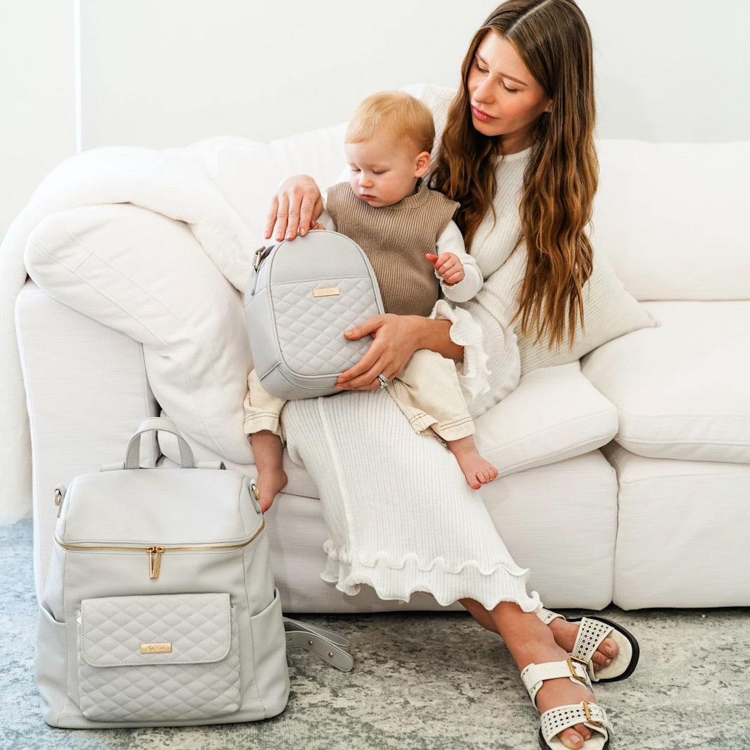 Mom holding baby showing Luli Bebe Stone Grey diaper bag and snack bag set – stylish and functional baby essentials for travel